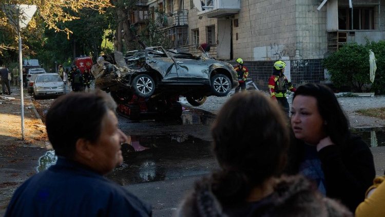 Pessoas observam um carro danificado ap&oacute;s um ataque russo em Kiev, em 20 de agosto de 2026, durante a invas&atilde;o da Ucr&acirc;nia pela R&uacute;ssia. O bombardeio russo matou seis pessoas e feriu dezenas na capital ucraniana e na regi&atilde;o circundante durante a noite, disseram as autoridades em 20 de agosto. (Foto de Tetiana DZHAFAROVA / AFP)