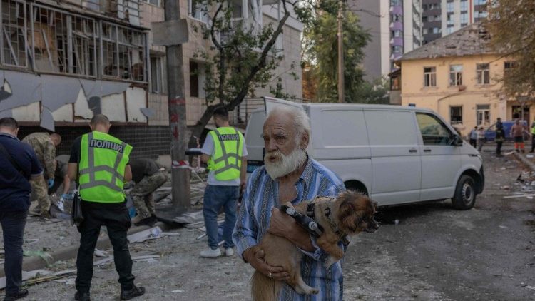 Um homem carregando um cachorro caminha ao lado de corpos de v&iacute;timas perto de um pr&eacute;dio residencial danificado em um ataque russo a Kiev, que tamb&eacute;m atingiu um hospital pr&oacute;ximo, em 20 de agosto de 2026, em meio &agrave; invas&atilde;o russa da Ucr&acirc;nia. Bombardeios russos mataram pelo menos 12 pessoas e feriram dezenas na capital ucraniana e na regi&atilde;o circundante durante a noite, disseram as autoridades em 20 de agosto. (Foto de Roman PILIPEY / AFP)