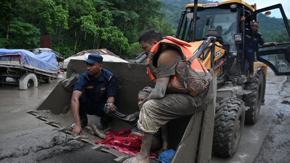 Equipes de resgate usam uma escavadeira para transportar uma pessoa afetada por enchentes repentinas em Devghat, no distrito de Nuwakot, Nepal, em 26 de agosto de 2026. Inundações de grandes proporções mataram oito pessoas no Nepal em 26 de agosto, enquanto a mídia estatal chinesa noticiava "grandes vítimas" devido a um deslizamento de terra em um centro comercial tibetano no lado chinês da fronteira compartilhada entre os dois países. (Foto de Prakash Mathema / AFP)