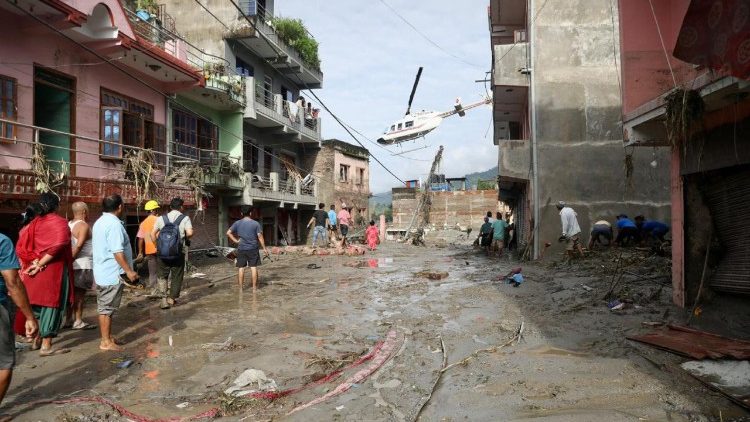 Gli abitanti osservano un elicottero sorvolare le case sommerse dal fango dopo le inondazioni improvvise a Devighat, nel comune di Bidur, nel distretto di Nuwakot, in Nepal