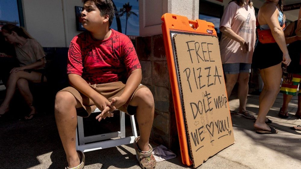 Um jovem está sentado ao lado de uma placa que diz 'Pizza grátis e Dole Whip We Love You' at Pizza Paradiso, em Lahaina, Havaí, EUA, 15 de agosto de 2023 (divulgada em 18 de agosto de 2023).