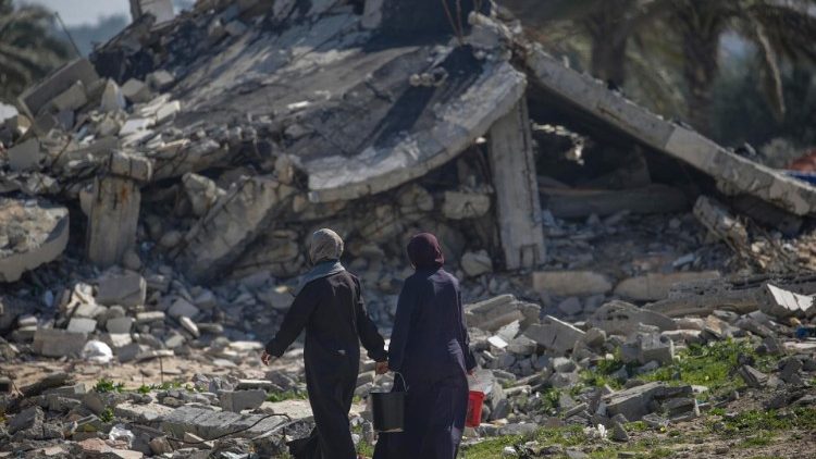 Displaced Palestinian women pass a destroyed structure in Deir Al Balah (From 2024)