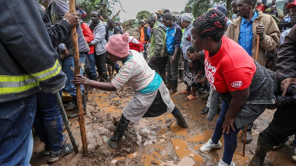 Moradores se reúnem para espiar enquanto voluntários e membros da Cruz Vermelha recuperam um corpo preso nos escombros durante uma operação de resgate em andamento após enchentes repentinas na aldeia de Kamuchira, em Mai Mahiu, Quênia, 30 de abril de 2024. (Daniel Irungu/Epa)
