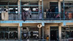 Internally displaced Palestinians look out from the balcony of a UNRWA school damaged by an Israeli airstrike