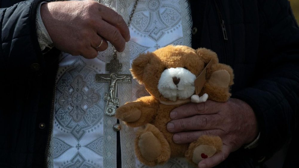 Sacerdote segura urso de pelúcia durante Missa de corpo presente de crianças mortas em ataque russo em Kryvyl Rih. EPA/MAXYM MARUSENKO