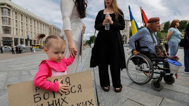 Uma menina ucraniana, Melania, de 1,9 anos, segura um cartaz durante um protesto em apoio às mulheres ucranianas capturadas e presas pela Rússia, pedindo às autoridades que devolvam seus parentes do cativeiro russo, na Praça da Independência, em Kiev, Ucrânia, em 19 de junho de 2025, em meio à invasão russa. EPA/SERGEY DOLZHENKO