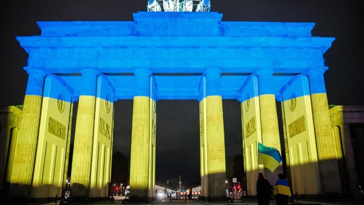 Participants with Ukrainian national flags walk in front of the Brandenburg Gate illuminated in Ukrainian national colors during a rally under the motto 'We stand with Ukraine for the future of Europe' in Berlin, Germany, 24 February 2026. Ukraine marks the fourth anniversary since Russia began its full-scale invasion of the country in 2022.  EPA/CLEMENS BILAN