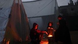 Displaced Palestinians, who fled their houses due to Israeli strikes, warm themselves by a fire on a rainy cold day at a tent camp, amid the ongoing conflict between Israel and Hamas, in Rafah