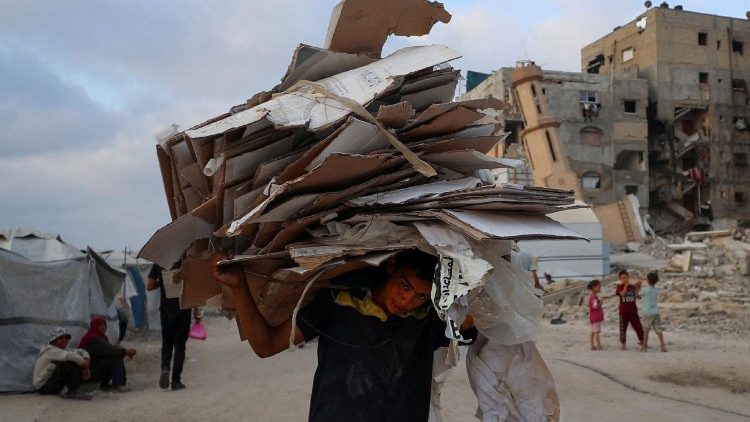 Um menino carrega papelão enquanto palestinos se reúnem para receber suprimentos de ajuda em Beit Lahia, norte da Faixa de Gaza, em 22 de junho de 2025. REUTERS/Mahmoud Issa