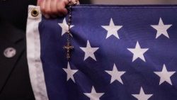 A man holds an American flag and a rosary at a vigil for Charlie Kirk in New York City