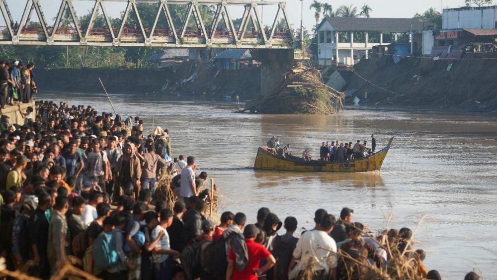 Pessoas atravessam um rio em um barco de madeira enquanto outras esperam, em uma área atingida por enchentes repentinas e mortais após fortes chuvas na Regência de Bireuen, Aceh, Indonésia, em 29 de novembro de 2025. REUTERS/Hendri