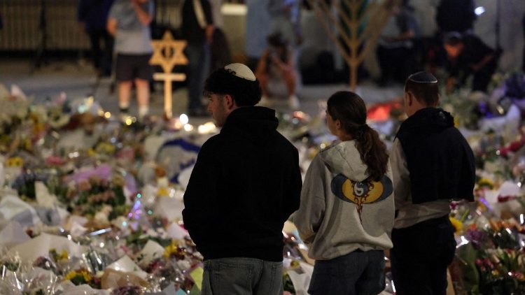 Persone in raccoglimento davanti ai fiori per le vittime dell'attentato di Bondi beach