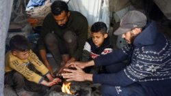 Civili palestinesi sfollati in tende di fortuna tentano di scaldarsi  