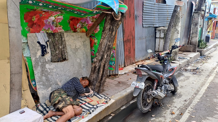 Une personne âgée endormie à même le sol aux Philippines.