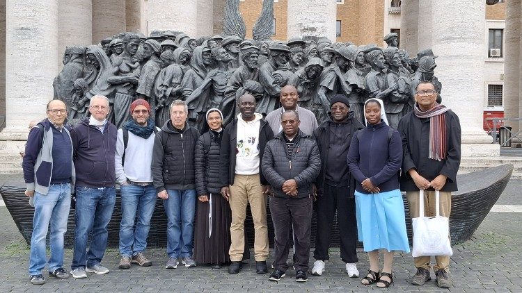 Na Praça de S. Pedro, diante da escultura, em bronze e barro, que retrata um grupo de migrantes de diversas culturas e diferentes períodos históricos.
