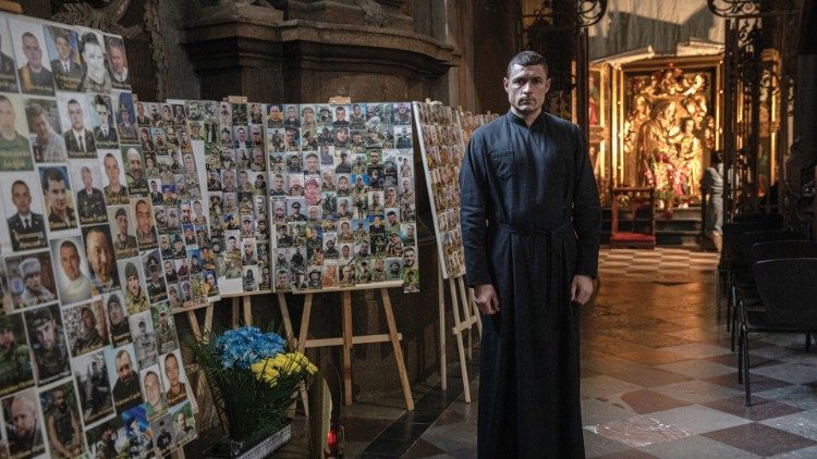 At Sts. Peter and Paul Garrison Church in Lviv., Father Andriy Khomyshyn stands next to photos of Ukrainian soldiers who died in the war against Russia. (photo: Konstantin Chernichkin)