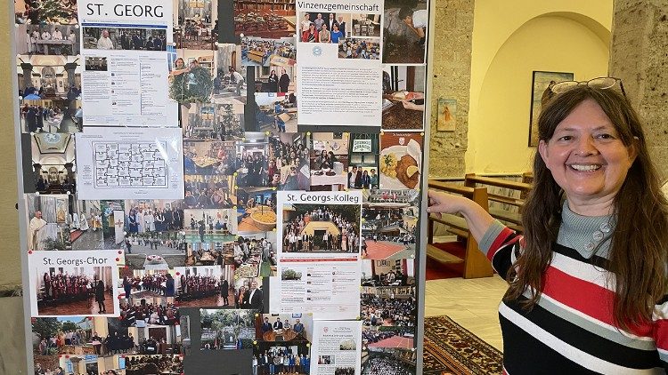 Gerda Willem vor dem Plakat, auf dem einige Aktivitäten der Gemeinde abgebildet sind