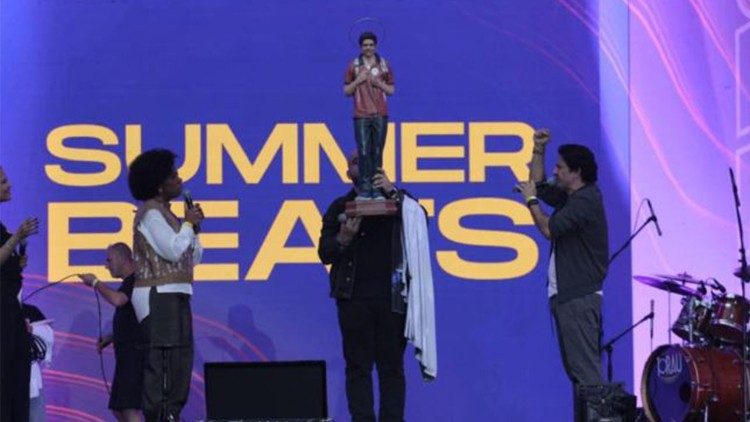 Pequena imagem de Carlo Acutis apresentada no palco aos participantes do Summer Beats