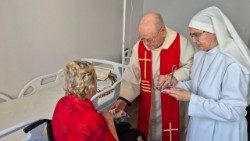 Padre Belmiro administrando a unção dos enfermos a uma idosa, acompanhado por uma Pequena Missionária